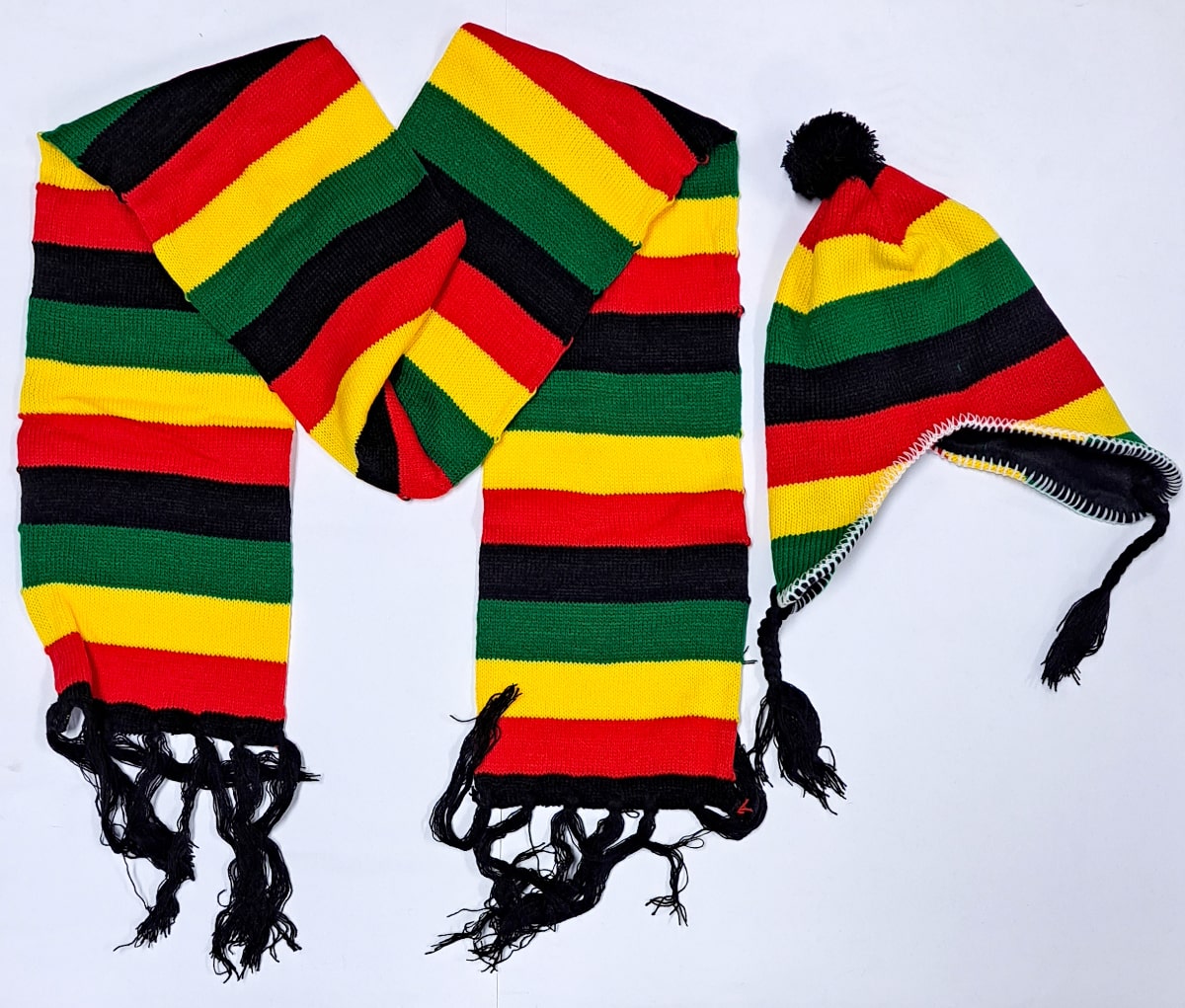 A knitted hat and scarf set in yellow, red, green, and black stripes. The hat has a pom-pom and ear flaps with tassels, and the scarf has fringed ends.