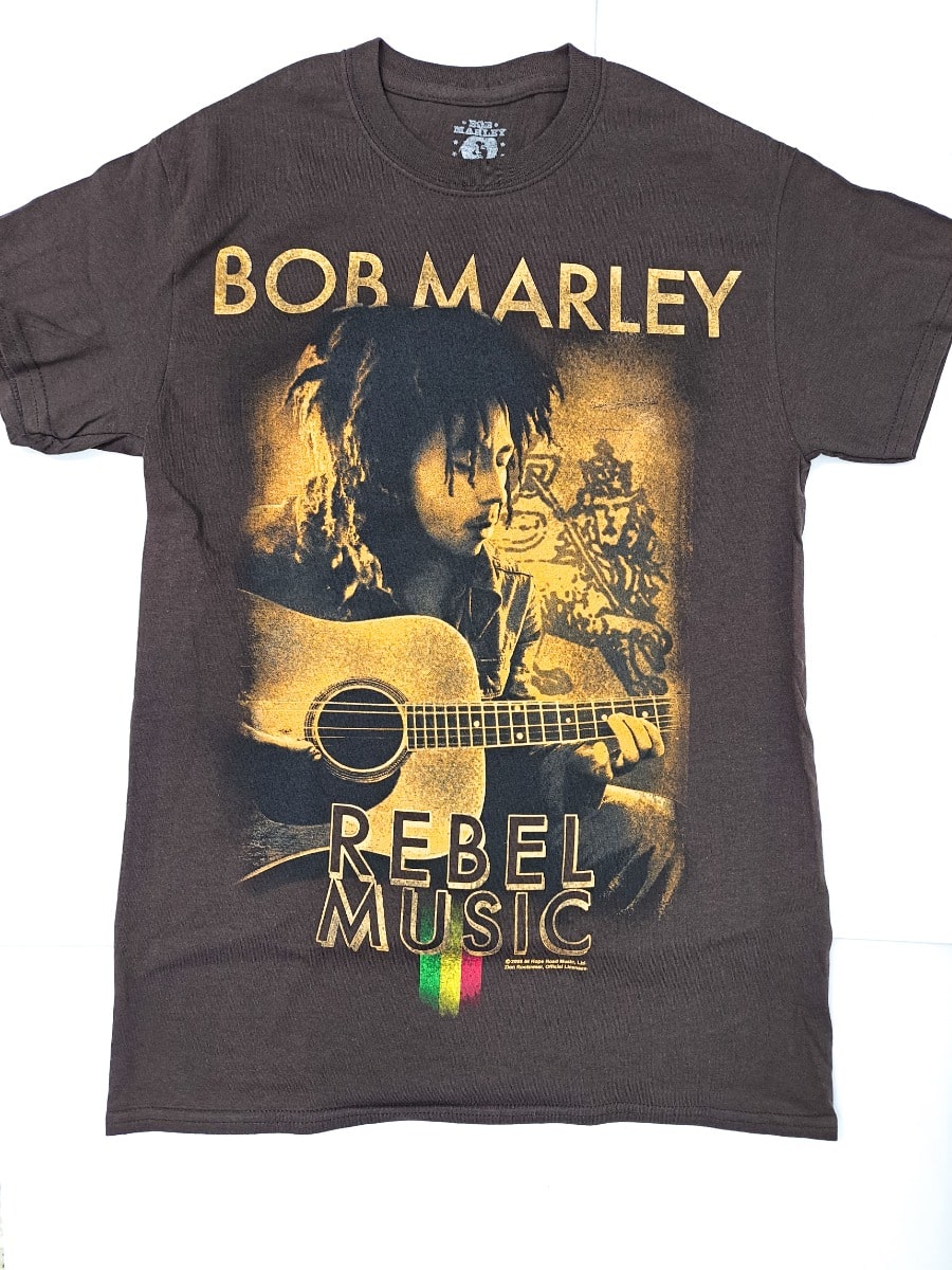 This 100% cotton brown T-shirt by 876 Worldwide features a captivating image of Bob Marley playing guitar, adorned with rasta-colored stripes and a symbolic gesture. Embrace the spirit of Rebel Music with this iconic tee.